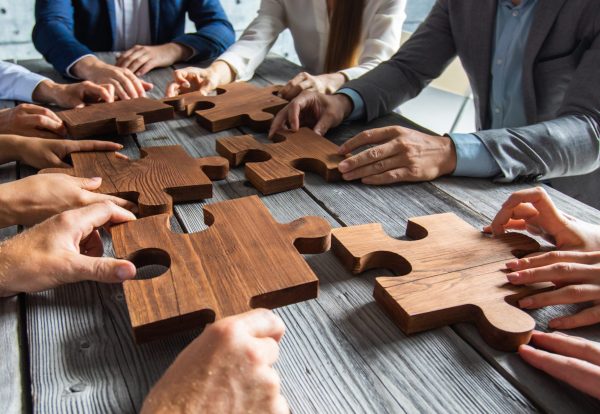 business-people-team-sitting-around-meeting-table-assembling-wooden-jigsaw-puzzle-pieces-unity-cooperation-ideas-concept-scaled.jpg